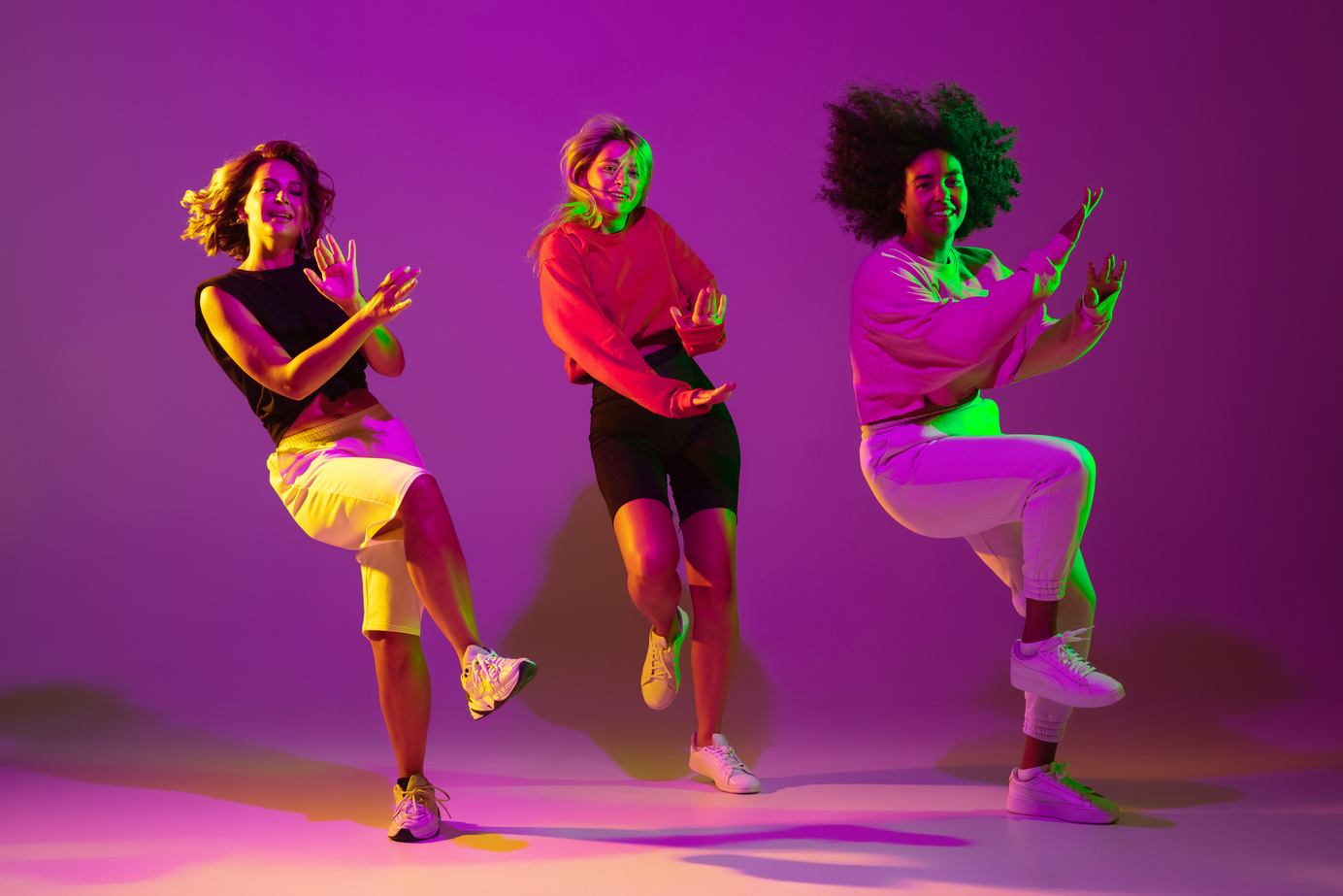 Sportive girls dancing hip-hop in stylish clothes on gradient background at dance hall in neon light