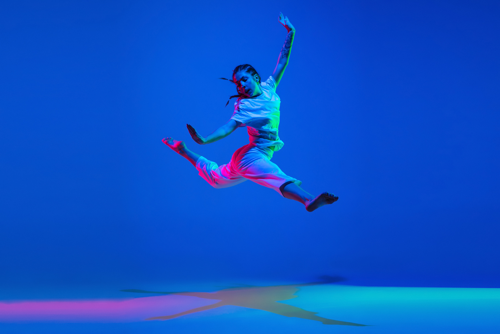 Young girl dancing hip-hop in white attire on colorful background in neon light