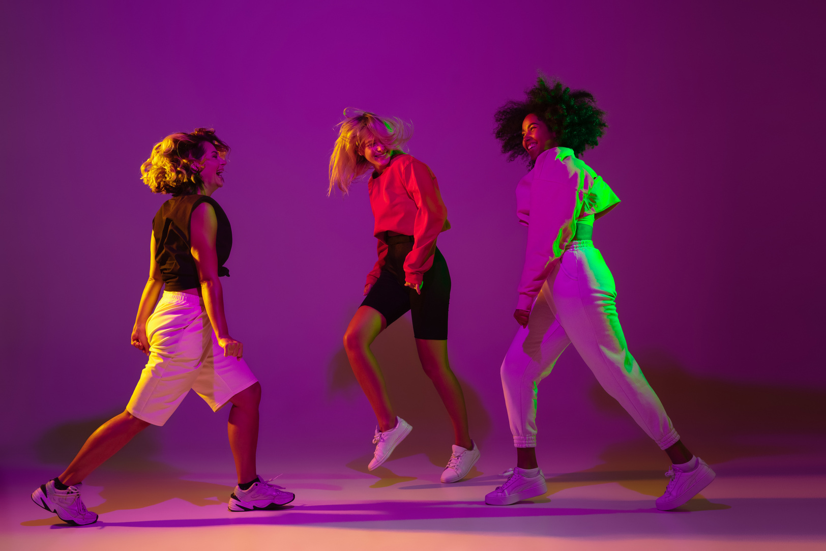 Sportive girls dancing hip-hop in stylish clothes on gradient background at dance hall in neon light